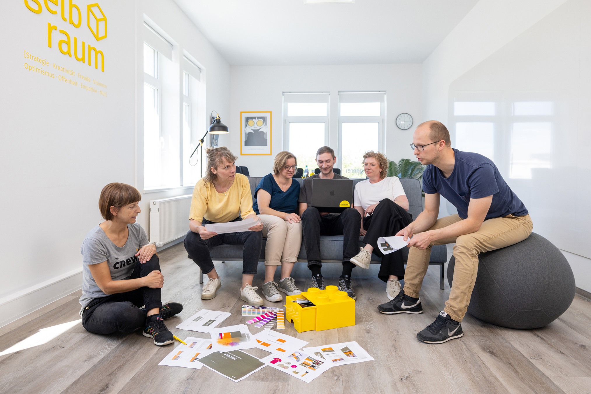 designerei-Team im gelbraum, versammelt um Entwürfe, besprechen Strategisches Design